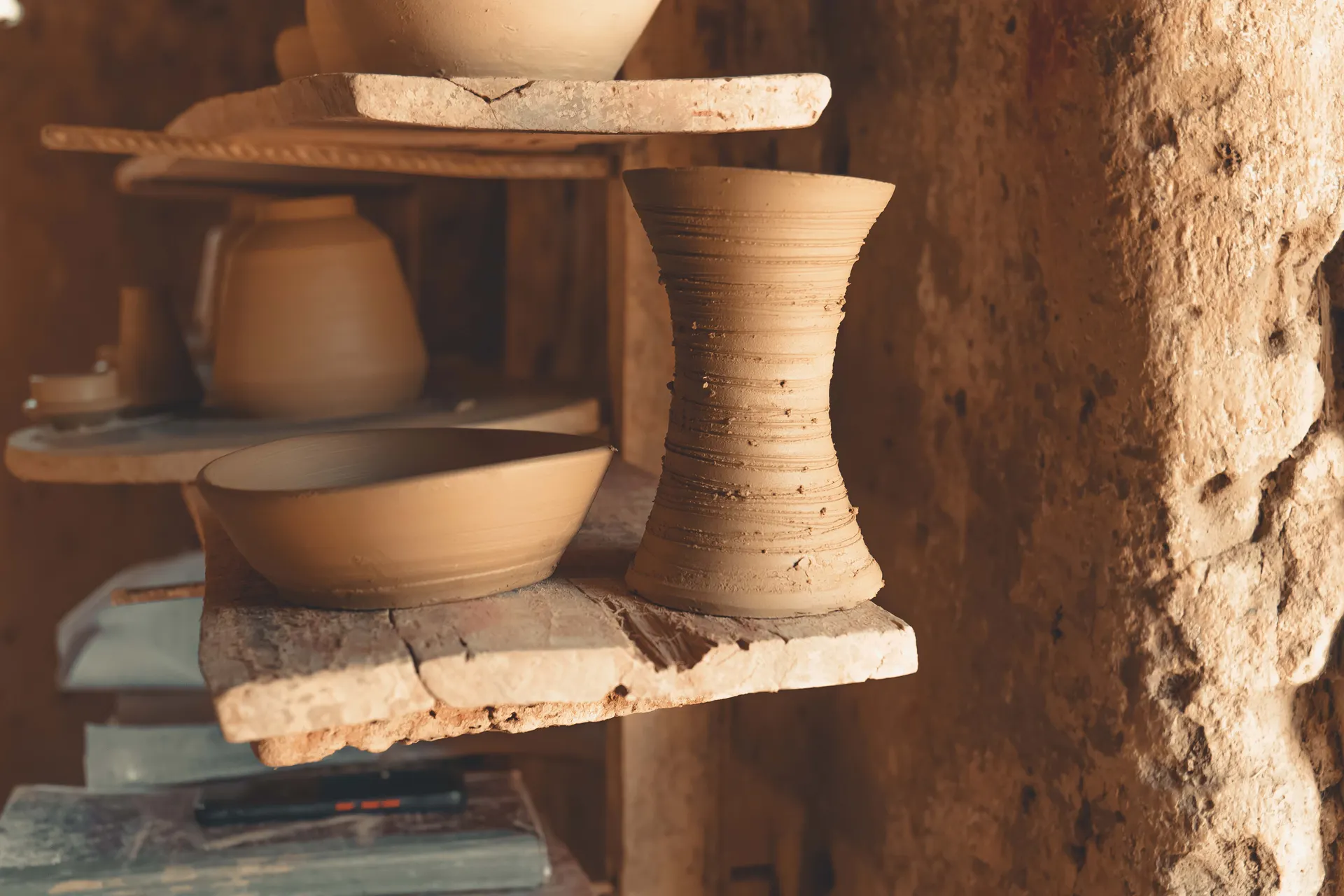 Handmade clay vessels on rustic wooden shelves.